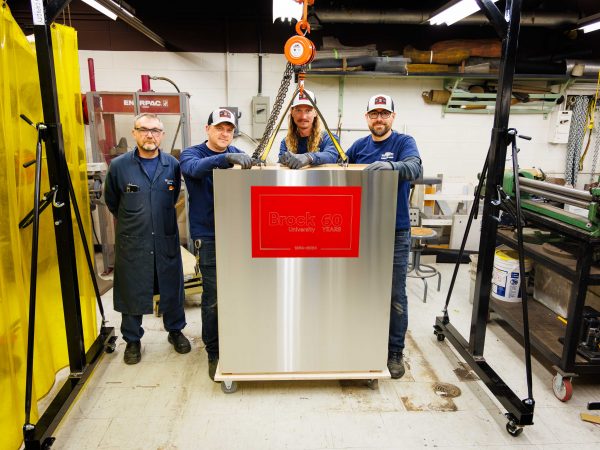Four members of Brock University’s Machine Shop team stand proudly with the completed time capsule created to mark the University’s 60th anniversary.