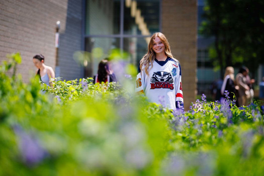 A young woman in a hockey jersey stands outside in a garden.
