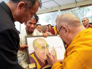 A young man gives the Dalai Lama a portrait painting as onlookers observe.