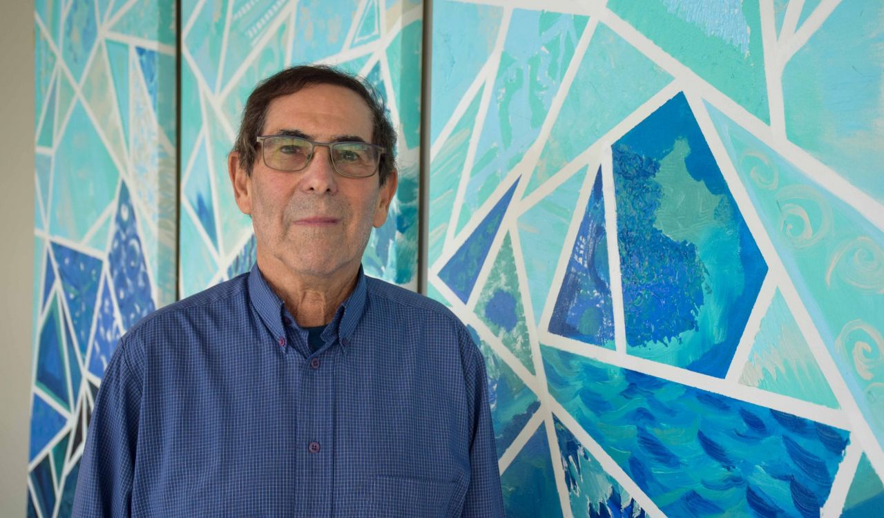 Maurice Feldman stands in front of a blue mural.