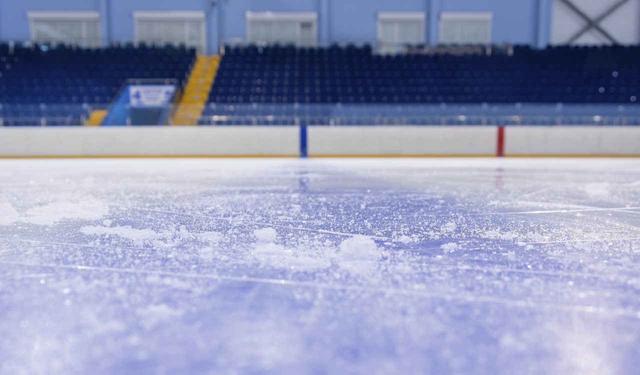 Close-up of an ice rink with empty arena seating in the background.