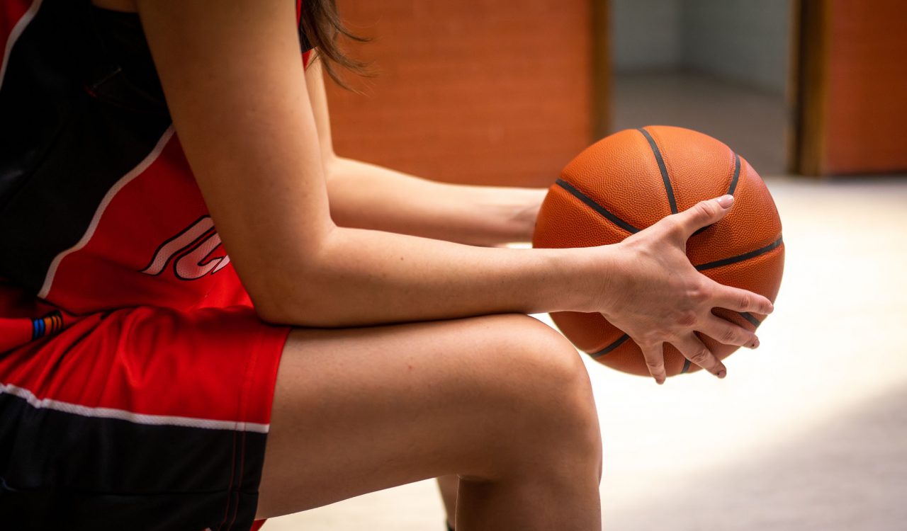 Close-up of a person in a uniform sitting on a bench holding a basketball.