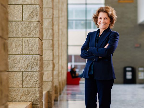 Woman in navy blazer with her arms crossed standing in hallway of a university.