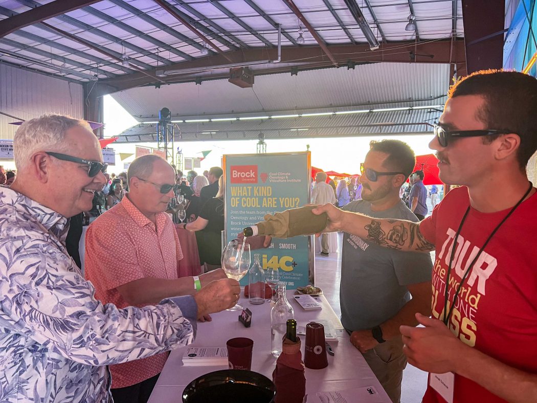 Two men pour wine tastings for guests at an event.