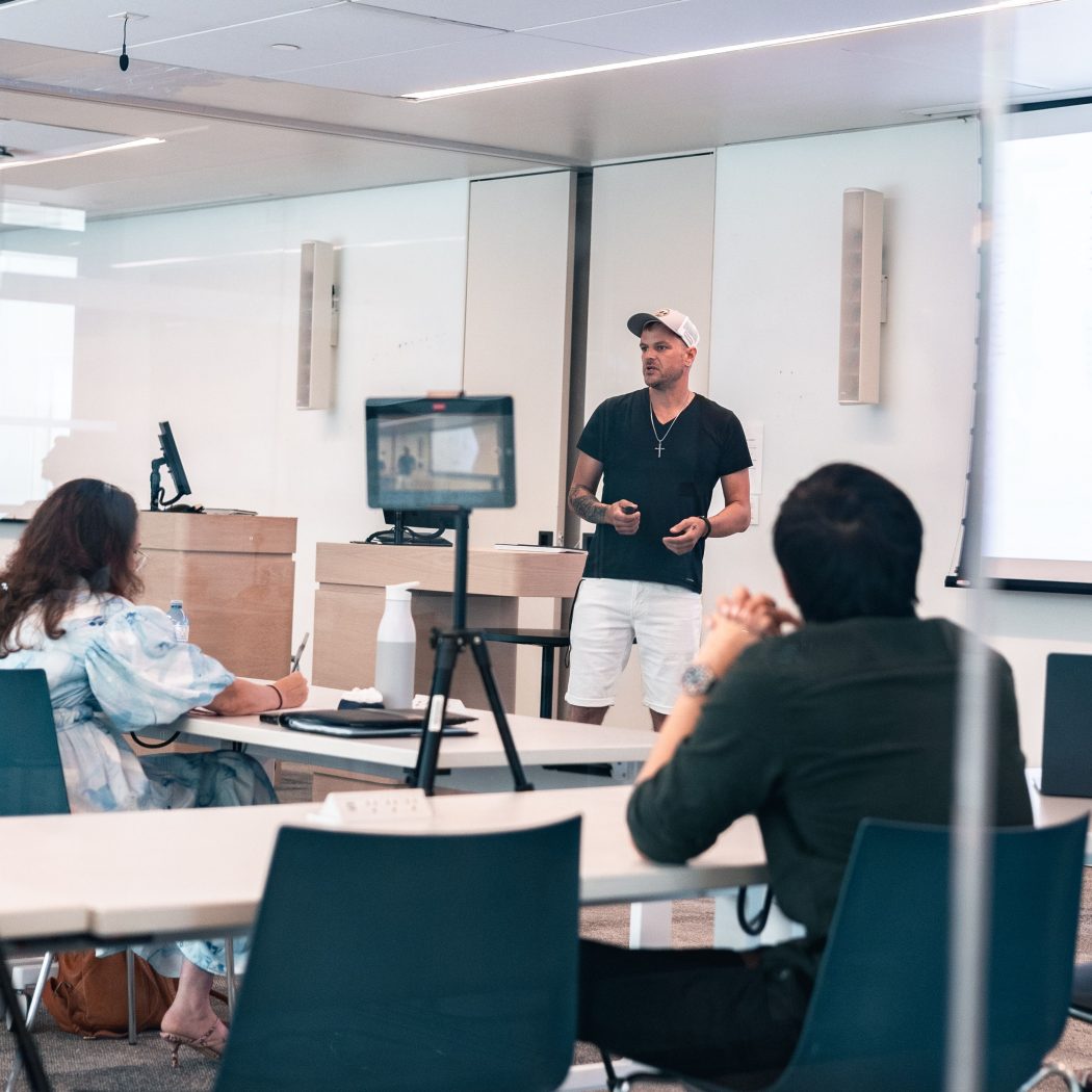 A man speaks to an audience in front of a screen,