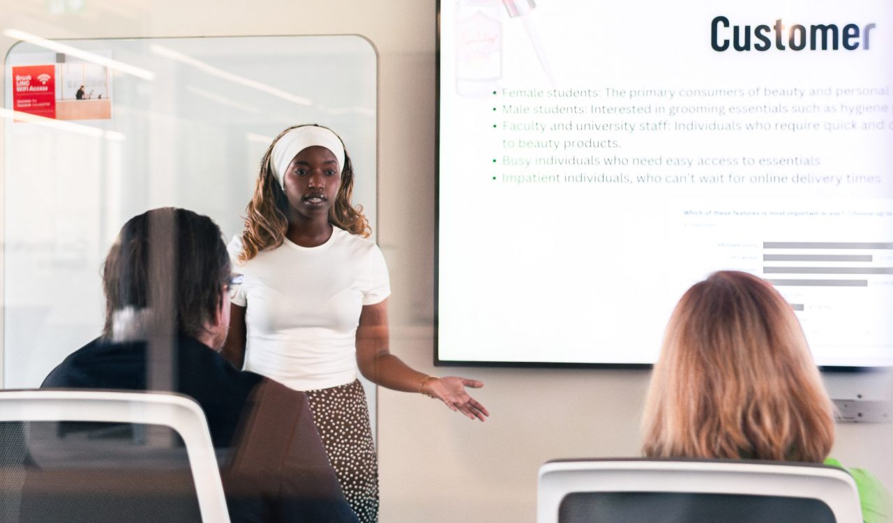 A woman speaks to an audience in front of a screen,