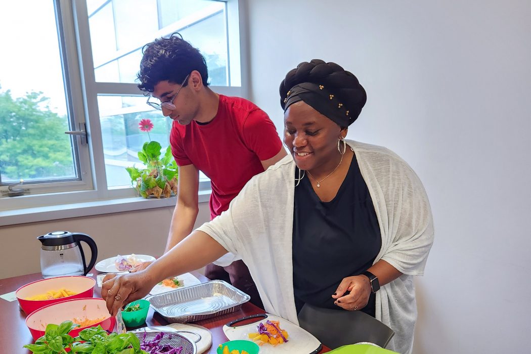 Two people make a meal in front of a window in a sunny room.
