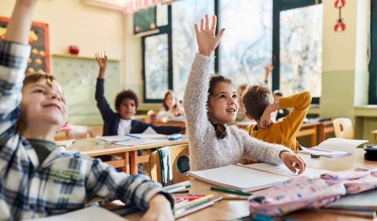 Elementary school students raise their hands in a classroom.