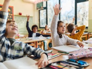 Elementary school students raise their hands in a classroom.