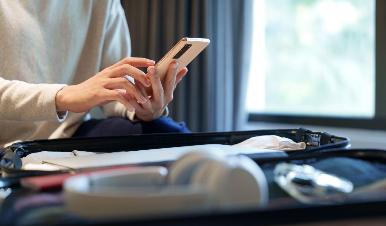 Close-up of hands holding a cellphone above an open suitcase.