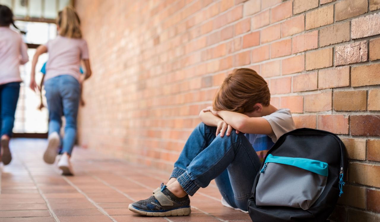 A child sits with their head in their arms in a school hallway.