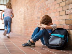 A child sits with their head in their arms in a school hallway.