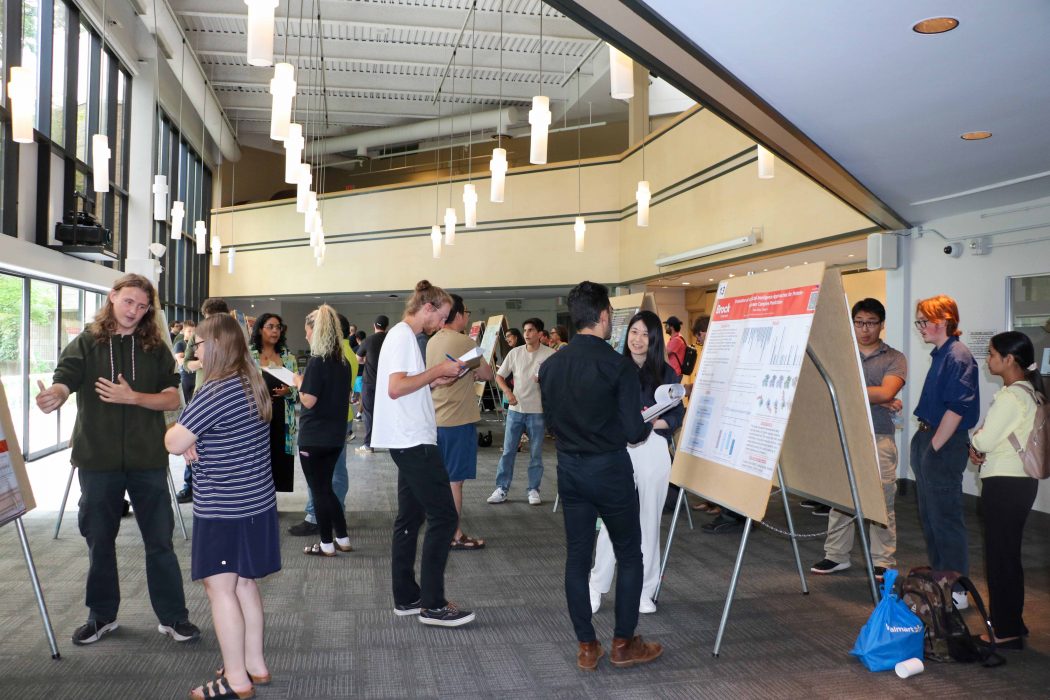 University students stand around presentation posters and chat in a large event space.