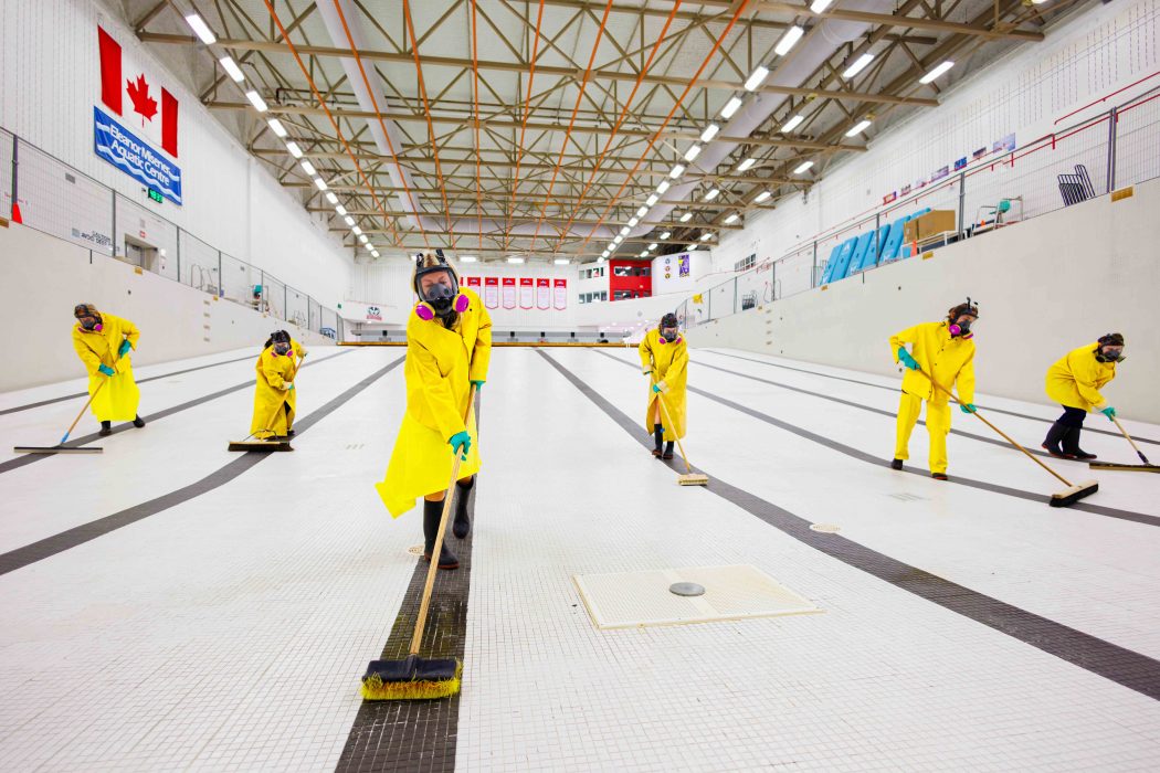 Staff wearing protective gear scrub the empty pool basin.