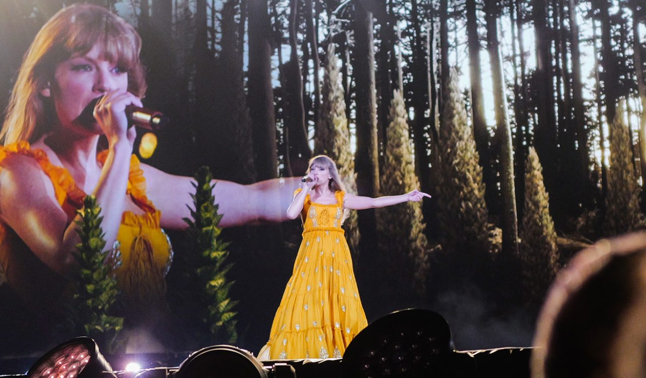 Taylor Swift wears an orange dress on stage during the Eras tour.
