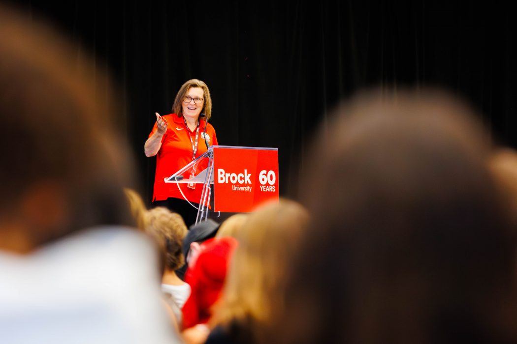 A Brock University leader addresses a packed gymnasium during Academic Orientation, speaking from a podium marked with the University’s 60th anniversary logo.