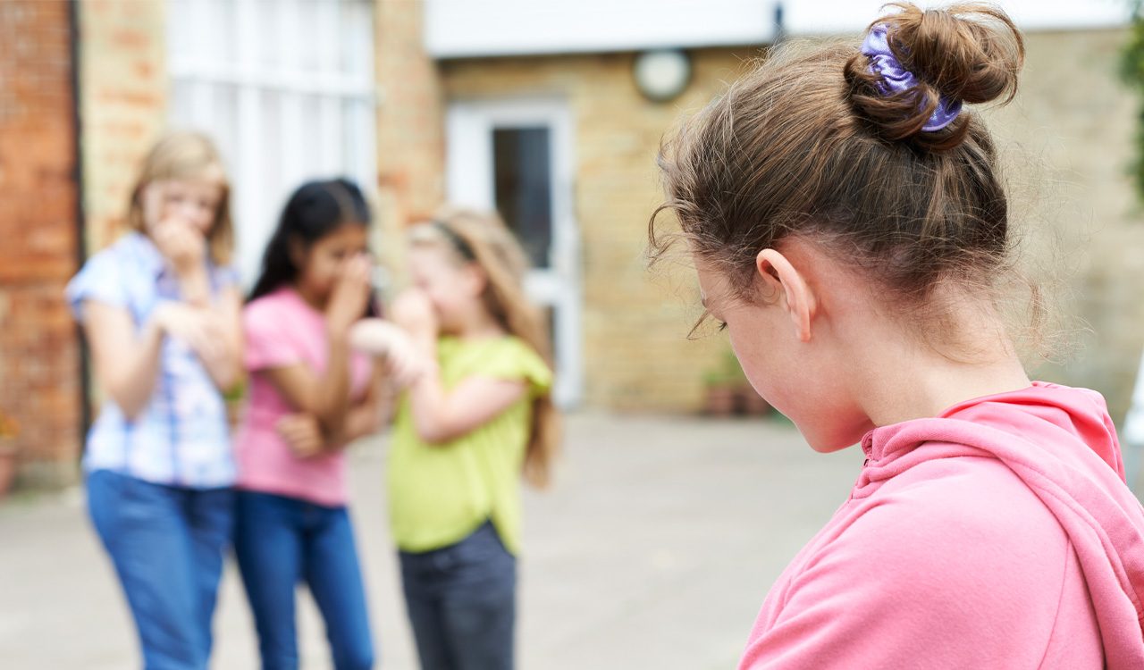 Girl in pink sweatshirt stands in front of group of girls laughing.