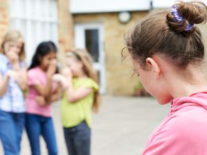 Girl in pink sweatshirt stands in front of group of girls laughing.