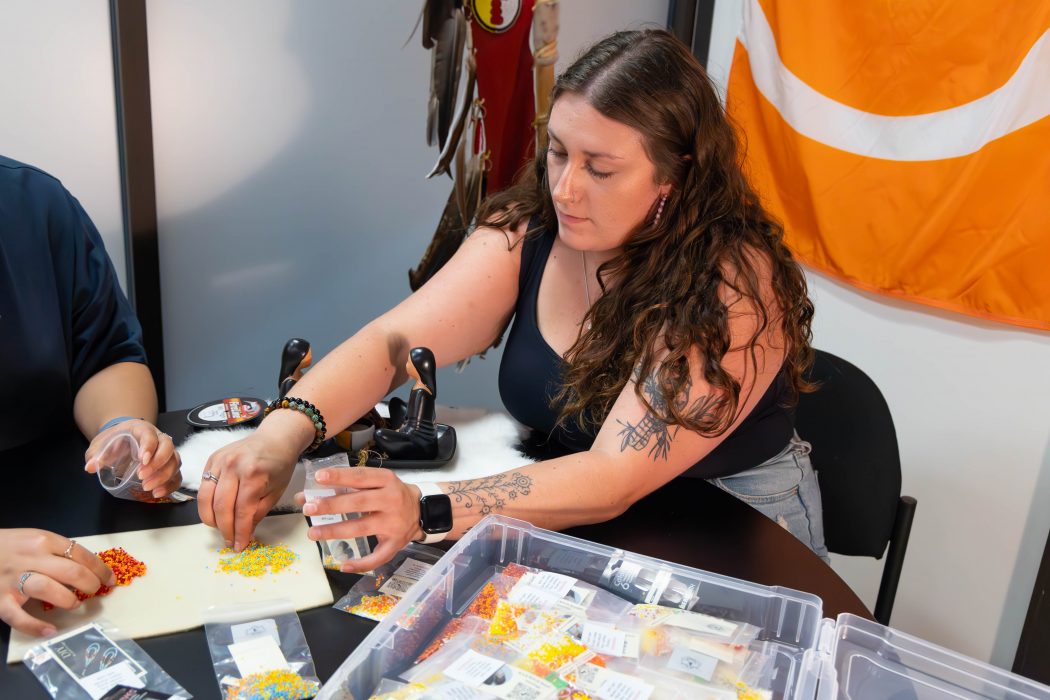 Woman picks up small coloured beads to put into plastic bags.