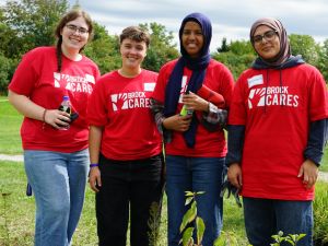 Four university students in red shirts stand in a field at a university volunteering event.