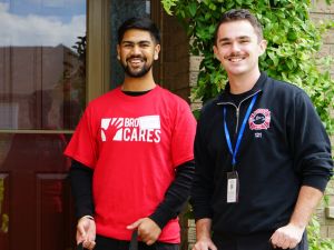 Two young men pose with red gift bags at a university volunteering event.