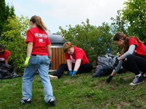 Three university students in red shirts do yardwork at a volunteering event.