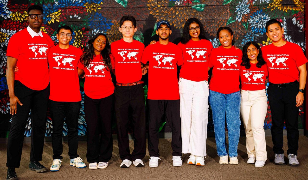 Brock International Student Ambassadors gather for a group photo, proudly wearing their red team shirts in front of a vibrant mural.