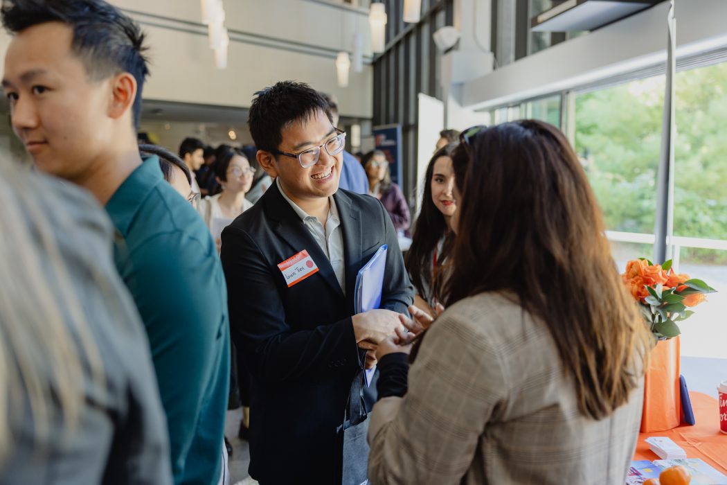 Student smiles while talking to a recruiter, a crowd of people are in the background.