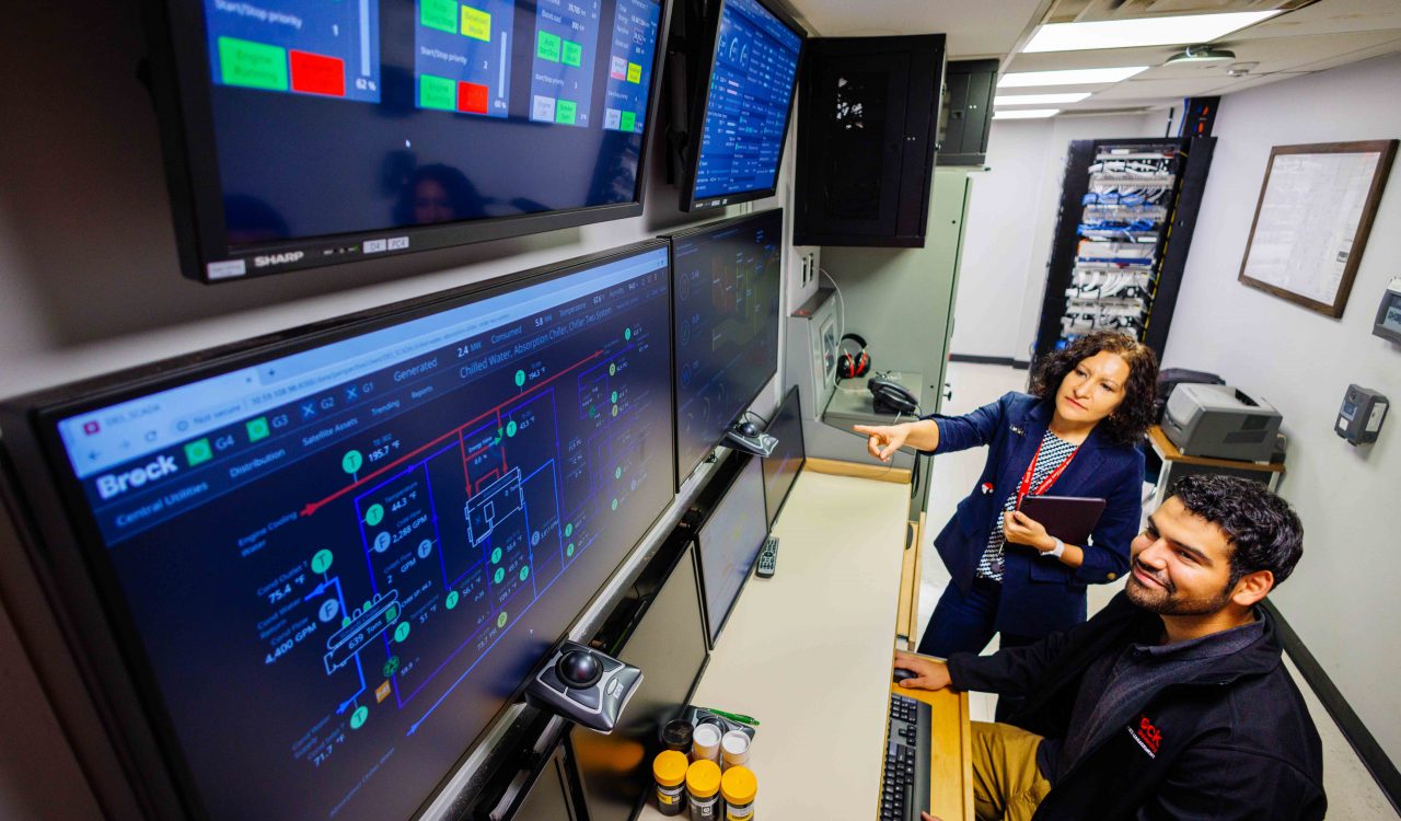 Two people look at a wall of screens.