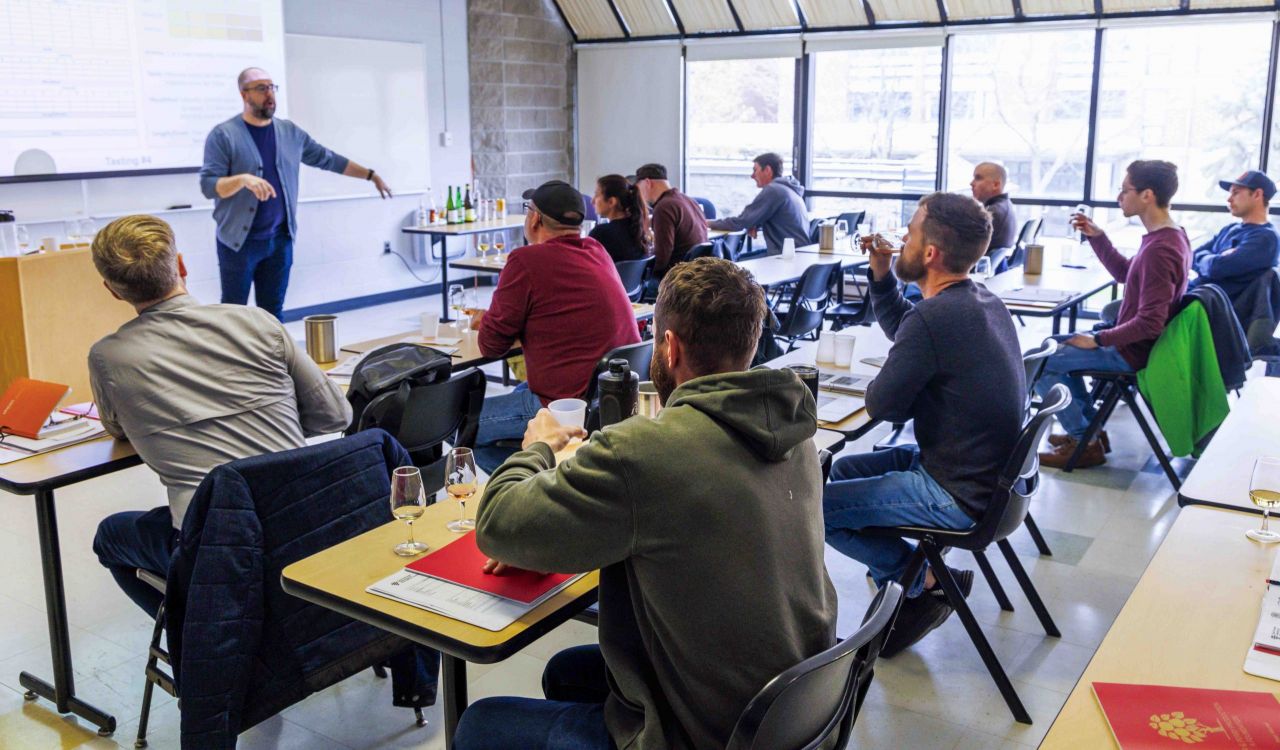 A group of people in a classroom taste cider during a training session.