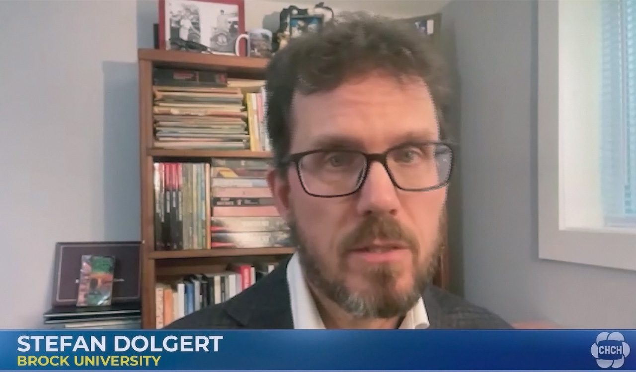Man does a television interview in front of a stack of books.
