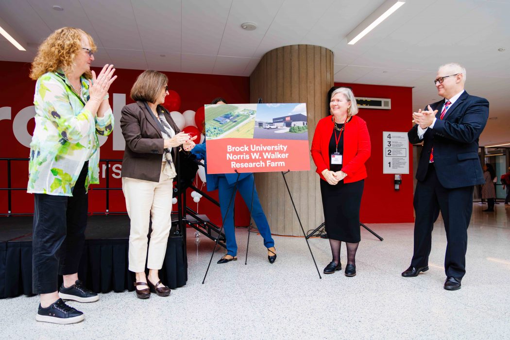 A group of people watch as a poster is unveiled at a university event.