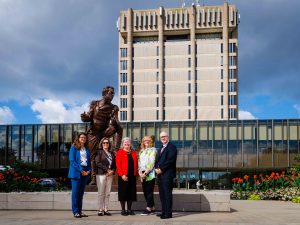Five people pose in front of a statue and the Schmon Tower at Brock University.