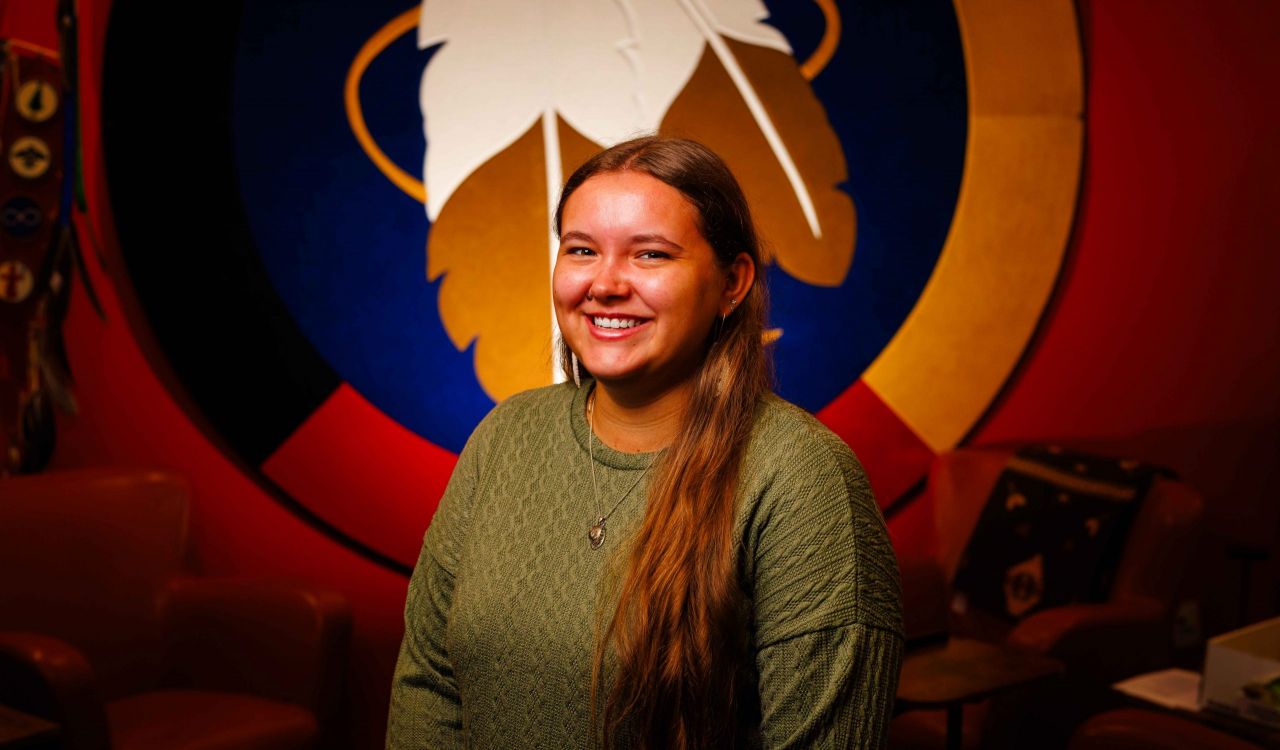 Woman stands in front of a wall hanging with feathers on it.
