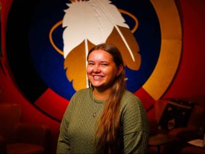 Woman stands in front of a wall hanging with feathers on it.