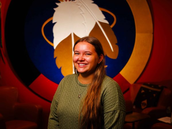 Woman stands in front of a wall hanging with feathers on it.