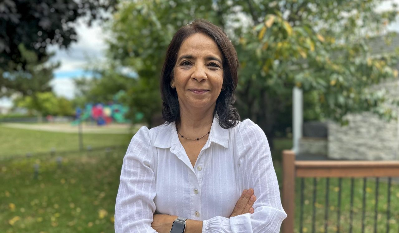 A smiling woman poses in a green space.