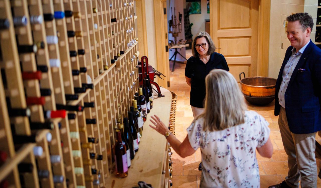A woman talks to another woman and a man in a wine cellar.