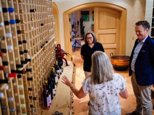 A woman talks to another woman and a man in a wine cellar.