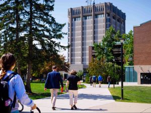 People walking on a university campus with a tall concrete building in the background.