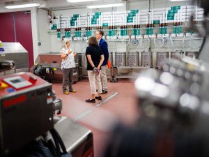 Group of three touring a winery production room with large equipment.