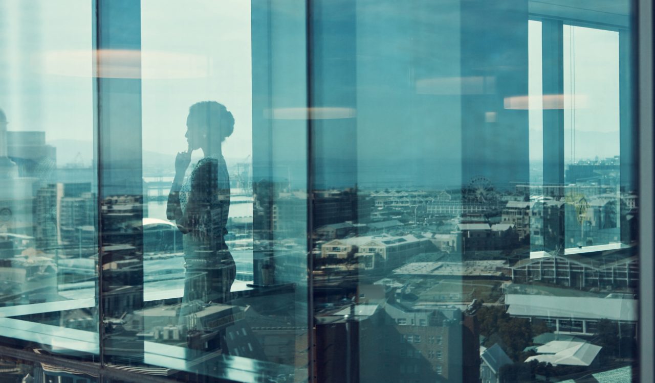A silhouette of a business woman seen through the window of an office building.