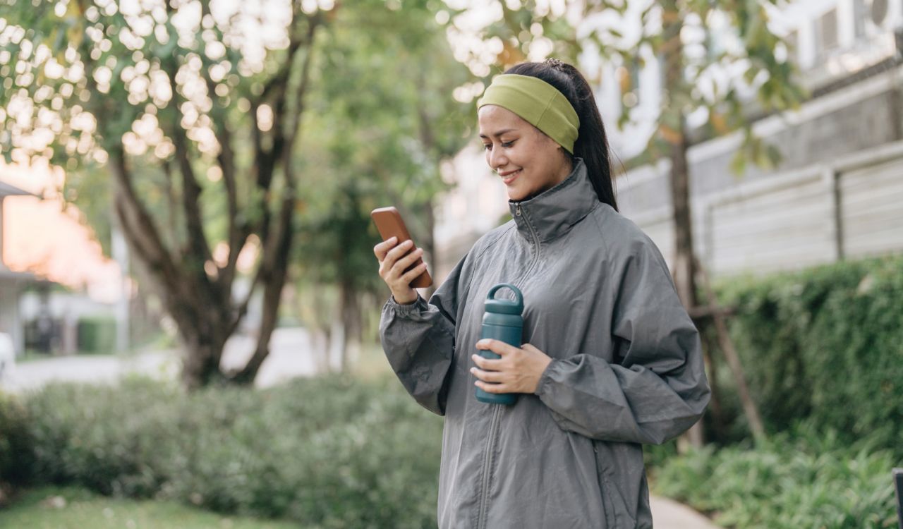 A woman looks at her phone while walking outside.