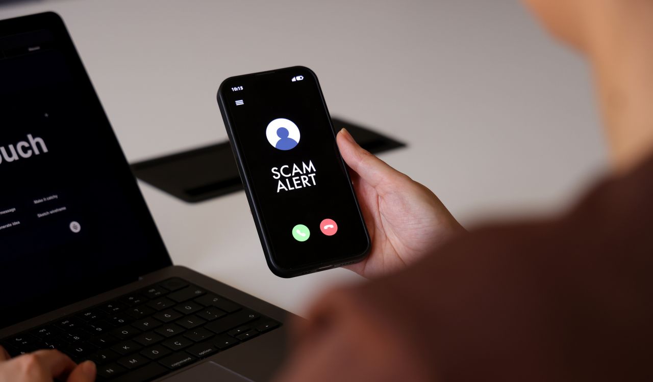 Close-up of hands holding a phone with "scam alert" on its screen.
