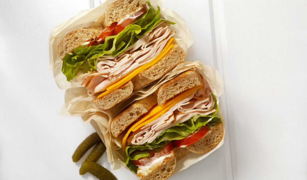 A deli sandwich sits on a table beside a few pickles.