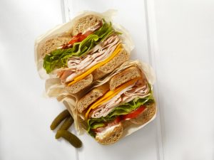 A deli sandwich sits on a table beside a few pickles.