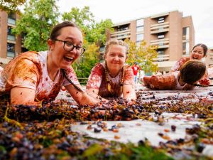 Two students crawling through grape pulp, smiling and covered in grape juice.