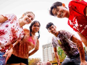 A group of four students in grape-stained shirts smiling and posing together.