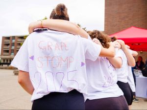 Students wearing custom shirts reading “Grape Stomp 2025” with arms around each other.