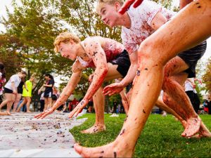 Two barefoot students crouching and getting ready to run across a grape-covered tarp.
